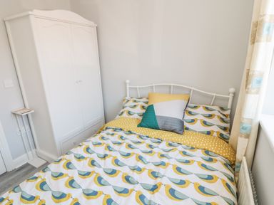 A bedroom with a bed with bird patterned bedding a white wardrobe and a small white stand at 20 Southmead in Amble