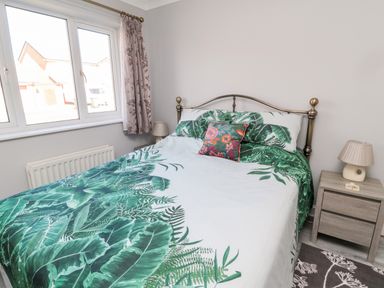 A bedroom with a bed with green leaf patterned bedding bedside tables with lamps and a window at 20 Southmead in Amble