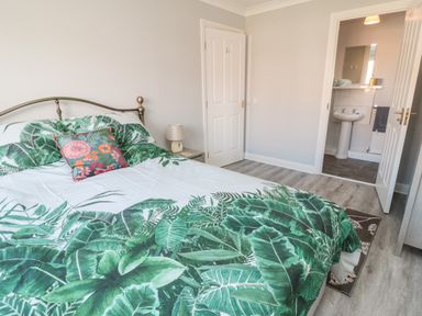 A bedroom with a bed and green leaf patterned bedding next to a bedside table with a lamp and an en suite bathroom at 20 Southmead in Amble