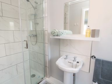 A bathroom with a shower, a pedestal sink, towels, a mirror, and soap dispenser at 20 Southmead in Amble