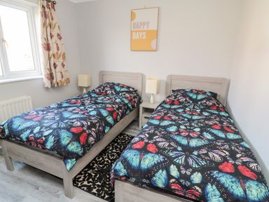 A bedroom with two beds covered in butterfly patterned bedding and a bedside table with lamps at 20 Southmead in Amble