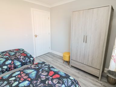 A bedroom with two beds with butterfly patterned bedding a wooden wardrobe a yellow stool and a white door at 20 Southmead in Amble
