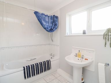 A bathroom with a bathtub a blue shower curtain a sink with soap and a window at 20 Southmead in Amble