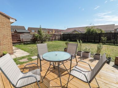 A backyard with a glass table and four chairs on a wooden deck at 20 Southmead in Amble