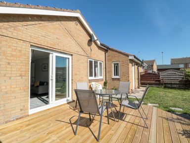 A patio with a glass table and four chairs outside a brick house at 20 Southmead in Amble