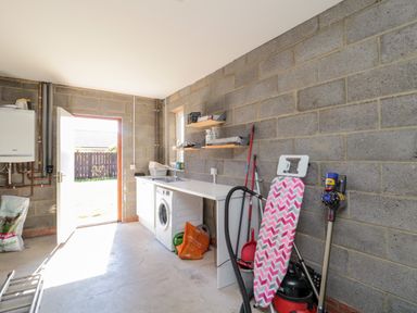 A utility room with an ironing board vacuum cleaner washing machine and sink at 20 Southmead in Amble