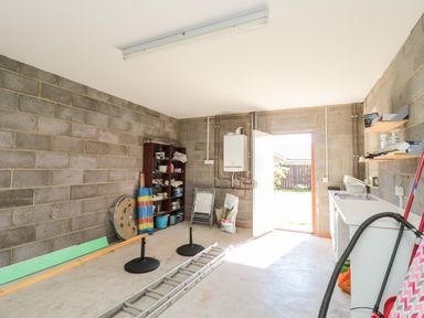 A utility room with a ladder on the floor shelves with tools and supplies a sink and washing machine near an open door at 20 Southmead in Amble