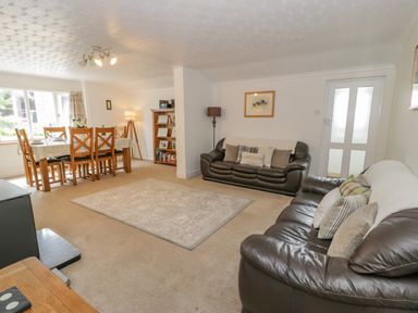 A living room with leather sofas a dining table with chairs a carpet and a bookshelf at Bwthyn Pengwern in Saron near Caernarfon