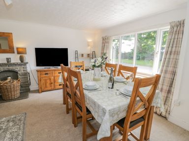 A dining room with a table set for six near large windows with curtains at Bwthyn Pengwern in Saron near Caernarfon