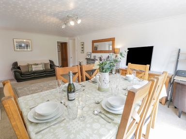 A dining table set with dishes glasses and a bottle in a living room with a sofa a television and a mirror at Bwthyn Pengwern in Saron near Caernarfon