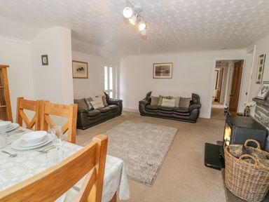 A living room with two leather sofas a carpet a dining table set with dishes a wood burning stove and a basket of logs at Bwthyn Pengwern in Saron near Caernarfon