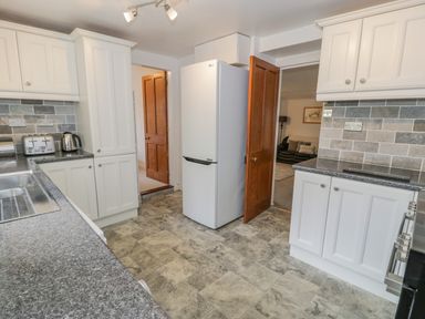 A kitchen with white cabinets a refrigerator a toaster and kettle on the counter at Bwthyn Pengwern in Saron near Caernarfon
