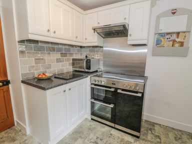 A kitchen corner with white cabinets a black and stainless steel oven a microwave on the counter and a bowl of apples at Bwthyn Pengwern in Saron near Caernarfon