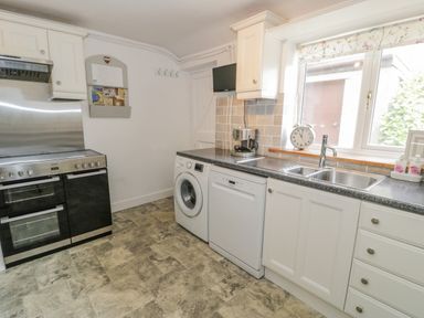 A kitchen with a black stove washing machine dishwasher and sink below a window at Bwthyn Pengwern in Saron near Caernarfon
