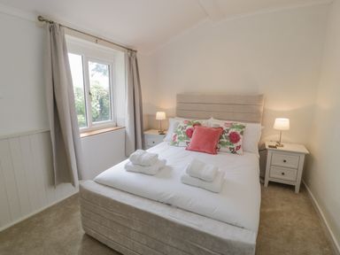 A bedroom with a double bed white bedding floral and pink cushions bedside tables with lamps and a window with curtains at Bwthyn Pengwern in Saron near Caernarfon