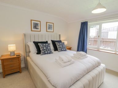 A bedroom with a bed with cushions and towels bedside tables with lamps and a window with blue curtains at Bwthyn Pengwern in Saron near Caernarfon