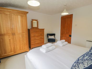 A bedroom with a bed towel sets wardrobe chest of drawers chair and wooden door at Bwthyn Pengwern in Saron near Caernarfon