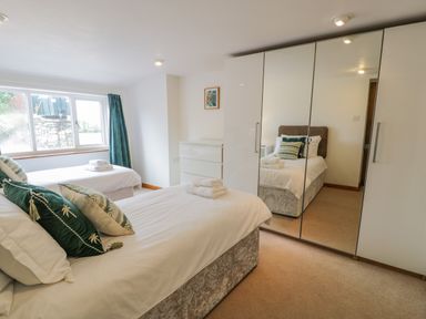 A bedroom with two single beds white bedding a white chest of drawers and a wardrobe with mirrored doors at Bwthyn Pengwern in Saron near Caernarfon