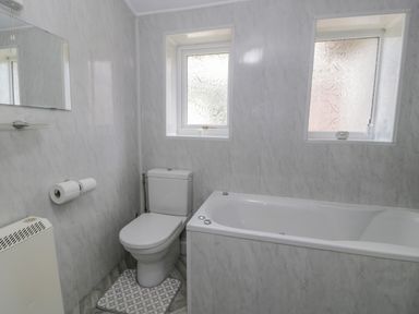 A bathroom with a toilet a bathtub two windows and a wall mirror at Bwthyn Pengwern in Saron near Caernarfon