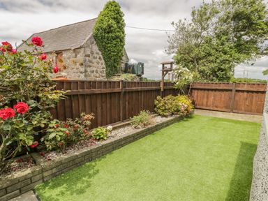 A garden with green grass a flower bed with red and white flowers a wooden fence and a stone building at Bwthyn Pengwern in Saron near Caernarfon