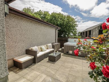 An outdoor patio with sofa seating a hot tub and flowering plants at Bwthyn Pengwern in Saron near Caernarfon