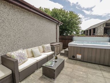 An outdoor patio with a wicker sofa set and a hot tub at Bwthyn Pengwern in Saron near Caernarfon