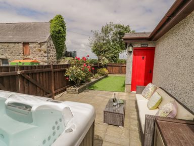 An outdoor patio with a hot tub sofa table with drinks red door and garden at Bwthyn Pengwern Saron near Caernarfon