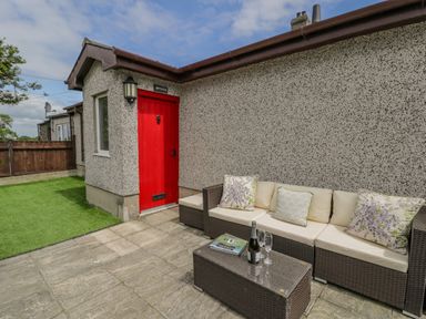An outdoor patio area with a red door and wicker sofa with cushions at Bwthyn Pengwern in Saron near Caernarfon