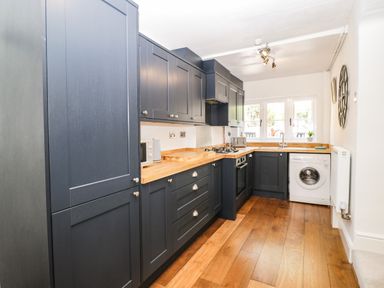 A kitchen with dark cabinets wooden countertops washing machine and window at Cuckoo Cottage in Upton Upon Severn
