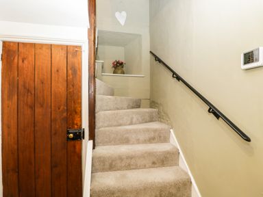 A carpeted staircase with a wooden door and a black handrail on the wall at Cuckoo Cottage in Upton Upon Severn