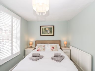 A bedroom with a bed with floral pillows and towels on it two bedside tables with lamps and a painting above the bed at Cuckoo Cottage in Upton Upon Severn