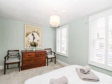 A bedroom with a wooden dresser and two chairs next to windows with white blinds at Cuckoo Cottage in Upton Upon Severn
