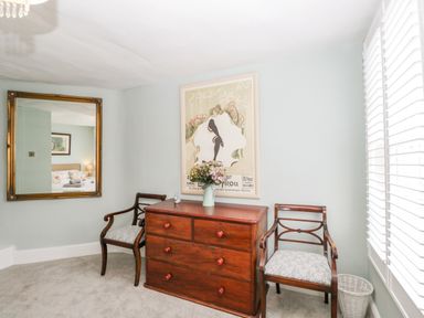 A room with a wooden chest of drawers with flowers on top two chairs on each side a large wall mirror and a framed picture on the wall at Cuckoo Cottage in Upton Upon Severn