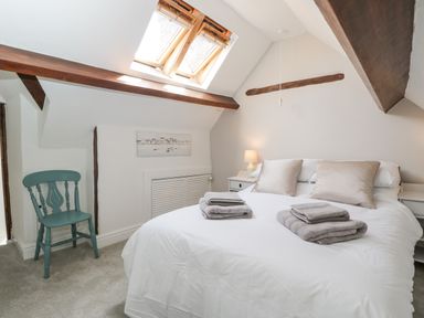 A bedroom with a bed pillows folded towels bedside tables lamp a blue chair and skylight windows at Cuckoo Cottage in Upton Upon Severn