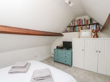 A bedroom with a bed folded towels a blue chest of drawers white cupboards and bookshelves at Cuckoo Cottage in Upton Upon Severn