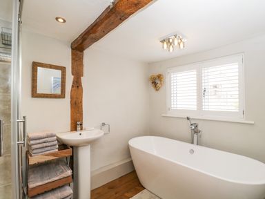 A bathroom with a freestanding bathtub sink wooden beam and folded towels at Cuckoo Cottage in Upton Upon Severn