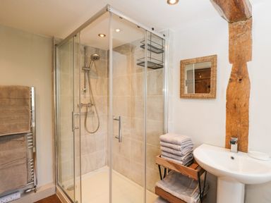 A bathroom with a glass shower enclosure towels on a rack and a sink with a mirror at Cuckoo Cottage in Upton Upon Severn
