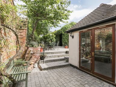 An outdoor patio with stone steps leading to a raised seating area with a table and chairs at Cuckoo Cottage in Upton Upon Severn