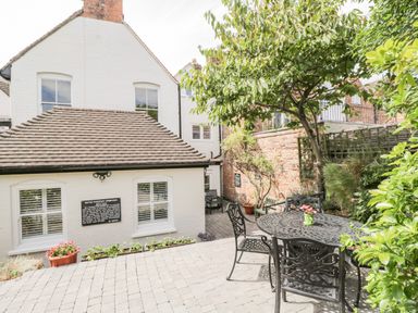 An outdoor patio with metal table and chairs next to a white building with windows and a tree at Cuckoo Cottage in Upton Upon Severn