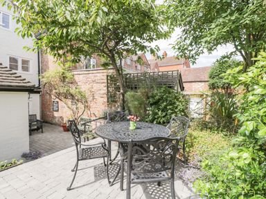 An outdoor patio with a round metal table and four chairs under a tree and surrounded by plants at Cuckoo Cottage in Upton Upon Severn