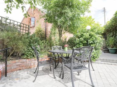 A patio area with a metal table and chairs surrounded by plants and a brick wall at Cuckoo Cottage in Upton Upon Severn