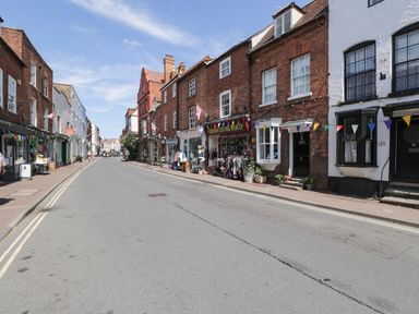 A street with shops and brick buildings on both sides with bunting strung across at Cuckoo Cottage in Upton Upon Severn