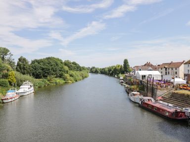 A river with boats docked along the shore and buildings on the right at Cuckoo Cottage in Upton Upon Severn