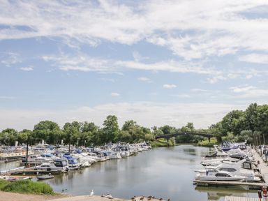 Boats docked on both sides of a river with a bridge and trees in the background