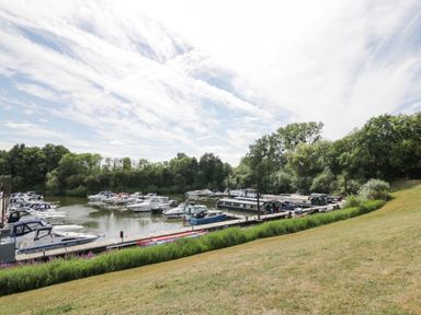 A marina with boats docked on the water near grassy land and trees at Cuckoo Cottage in Upton Upon Severn