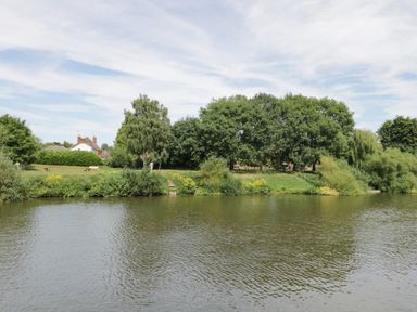 A river with trees and grass on the bank with houses in the background at Cuckoo Cottage in Upton Upon Severn