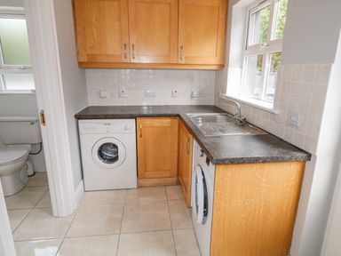 A small utility room with wooden cabinets a washing machine a sink and a view into a bathroom at 12 Hillview Ludden near Buncrana