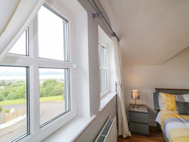 A bedroom corner with two windows a grey bedside table with a lamp and part of a bed at 12 Hillview Ludden near Buncrana