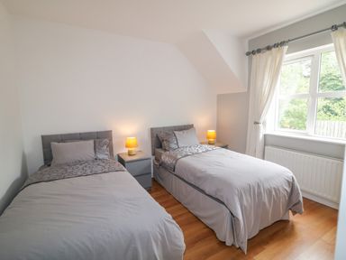 A bedroom with two single beds with grey bedding two bedside tables with lamps and a window with curtains at 12 Hillview Ludden near Buncrana