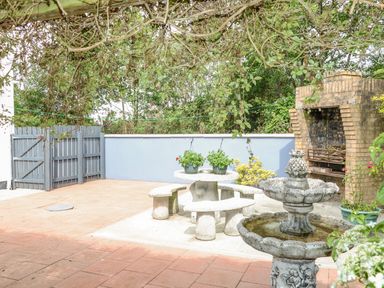 An outdoor patio with a stone table and benches potted plants a brick barbecue and a water fountain at 12 Hillview Ludden near Buncrana